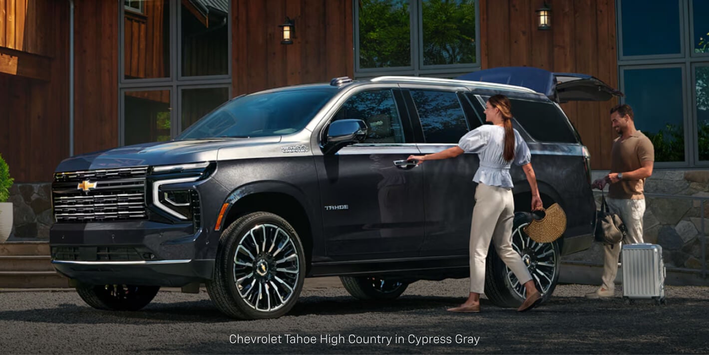 Three-quarter front view of a Chevrolet Tahoe High Country in Gray as a couple loads luggage.