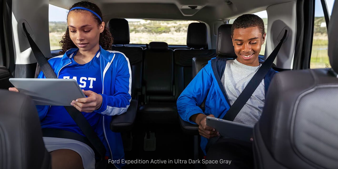 Interior cabin view of a Ford Expedition Active showing two teens using handheld tablets in the second-row.