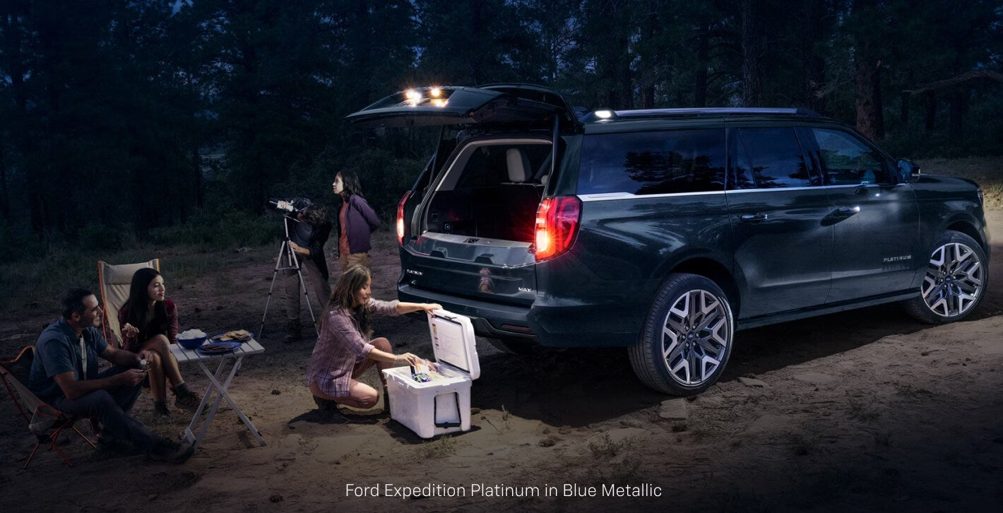 Side view of a Ford Expedition Platinum in Blue with people gathered around the open splitgate at night.